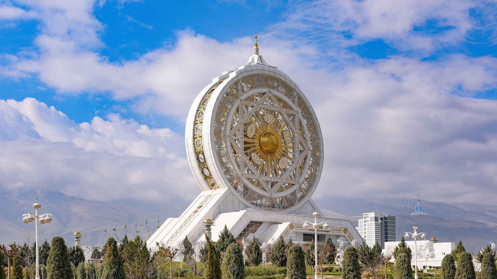 A large white and gold structure with a circular design, surrounded by trees and buildings. 2