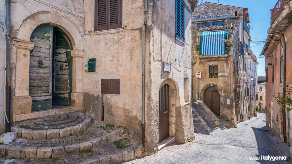A narrow street with historic buildings, stone steps, and a blue-striped awning. 2