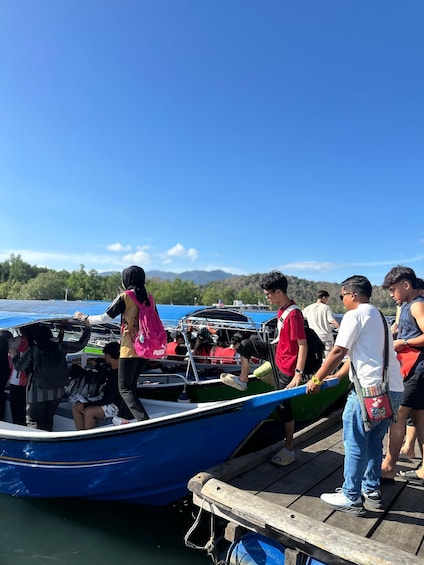 A group of people boarding a blue boat at a dock with a clear blue sky and mountains in the background. 1