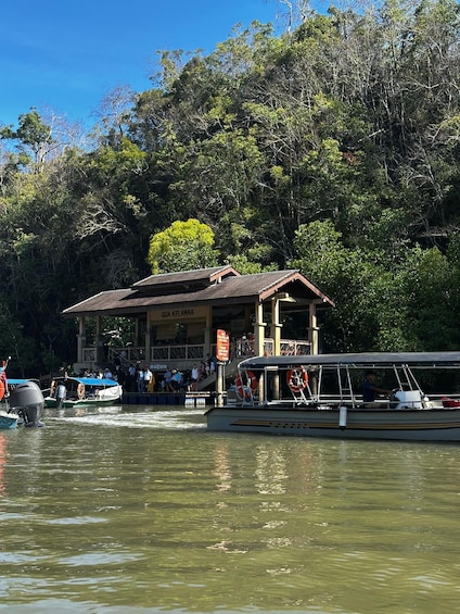 A boat docked near a wooden structure with a sign reading 'GUA KELAWAR' amidst a forested area. 5