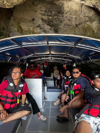 A group of people on a boat tour inside a cave, wearing life jackets and seated on the boat's floor. 4