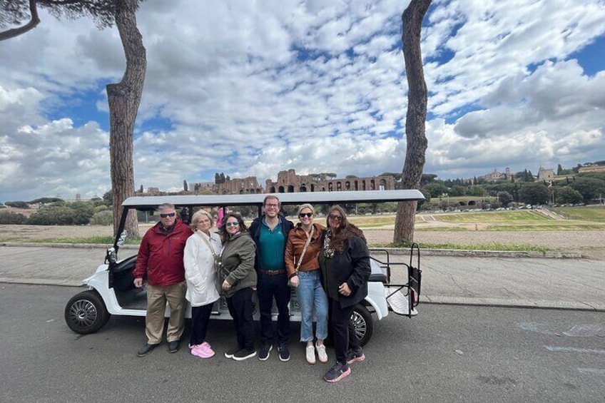 A group of people posing in front of a white golf cart with a historic building in the background. 3