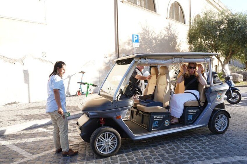 A golf cart with passengers, parked on a cobblestone street, a building, and a bicycle in the background. 4