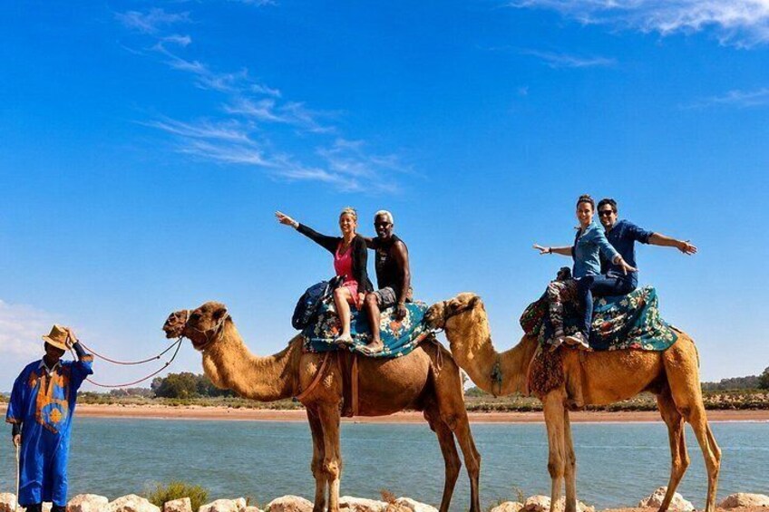 A group of people riding camels by a body of water. 2