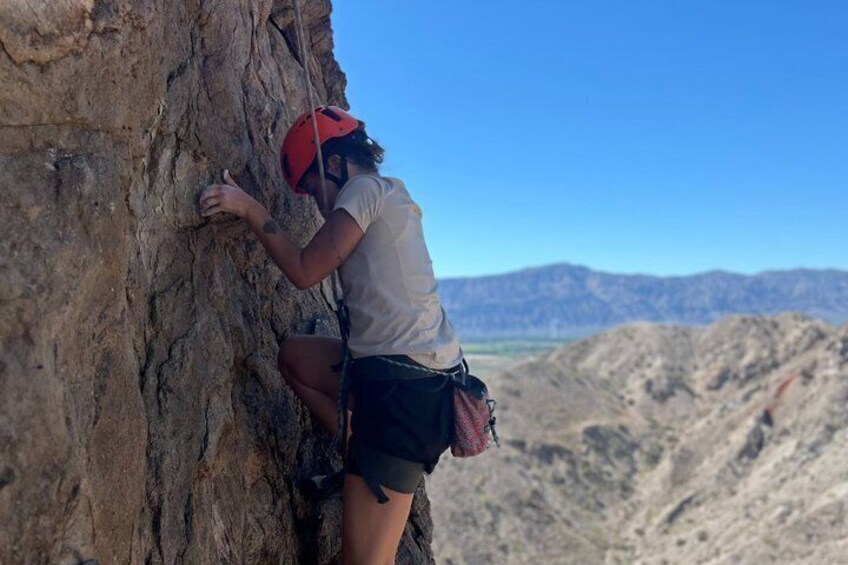 A person climbing a rocky cliff with a clear sky and mountains in the background. 2