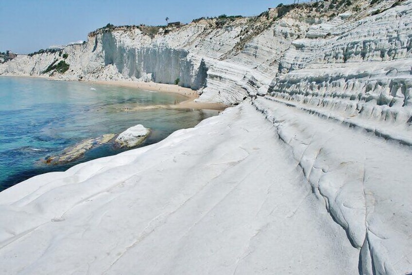 A white sandy beach with layered cliffs and clear blue water. 4