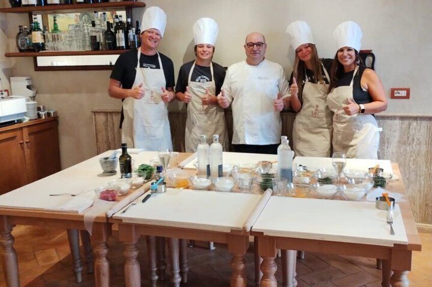 A group of chefs in aprons and chef hats standing around a table with cooking ingredients and utensils. 1