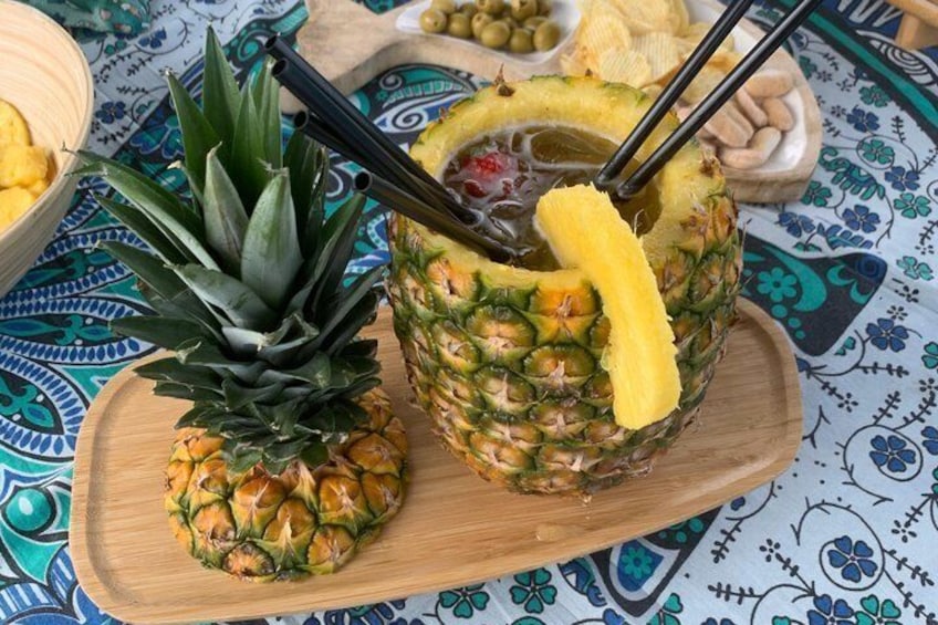 A pineapple and a drink on a wooden board with a patterned tablecloth. 4