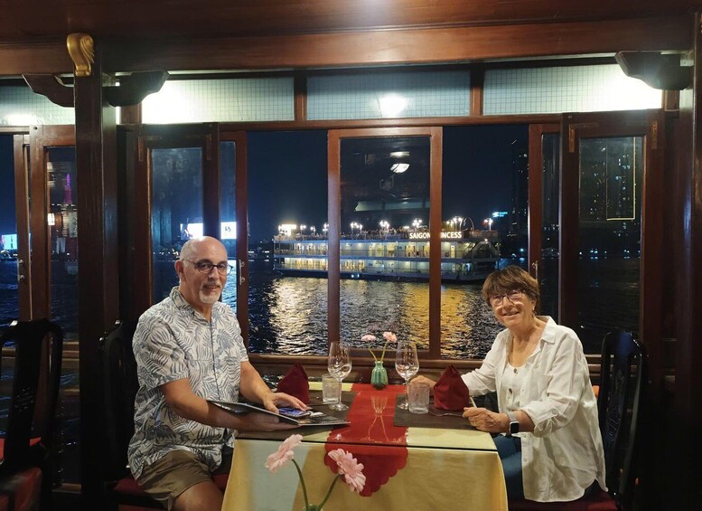 Two people dining at a table with a view of a river and a boat named 'SAIGON PRINCESS' in the background. 3