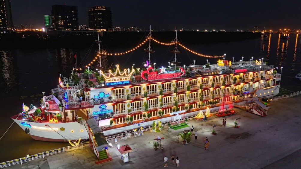 A brightly lit riverboat with multiple decks and festive decorations, docked at a waterfront. 5
