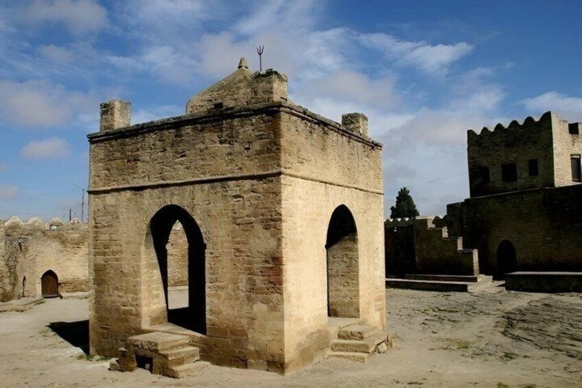 A historical stone structure with arches, a tower, and a castle-like building in the background. 2