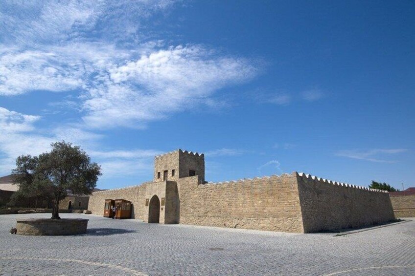 A historic stone wall with a tower, a paved courtyard, and a tree. 1