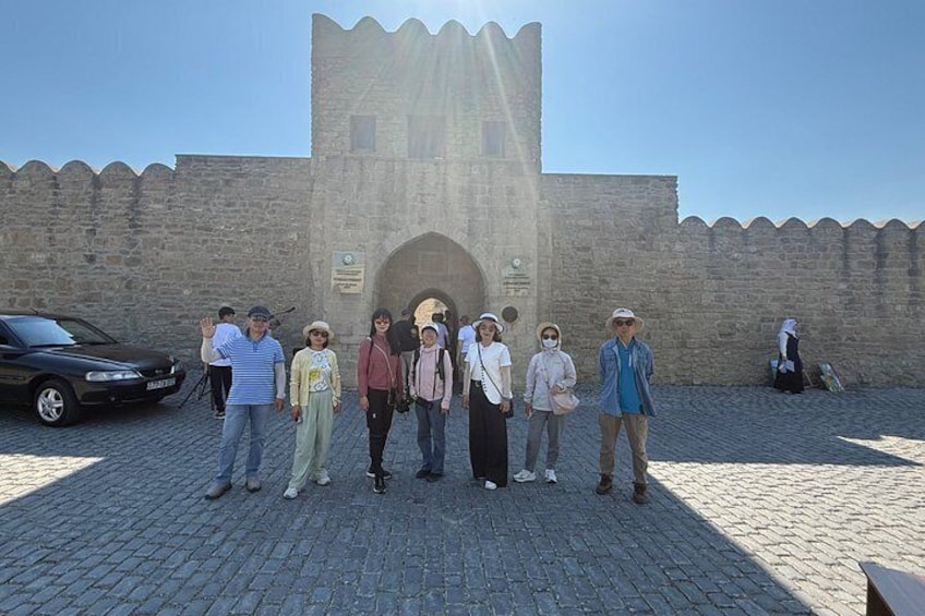 A group of people standing in front of a historic stone wall with a tower. 1