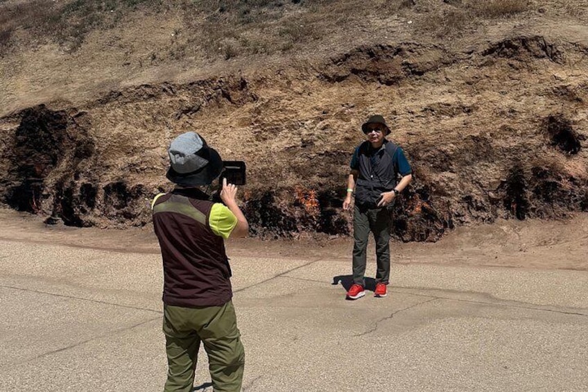 A person taking a photo of another person standing on a road with a hilly background. 3
