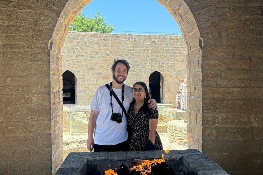 Two people standing in an ancient stone structure with a fire pit in the foreground. 2