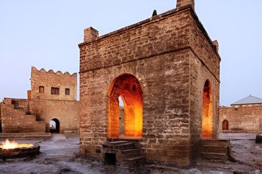 A stone building with arched openings and a fire burning in front. 5