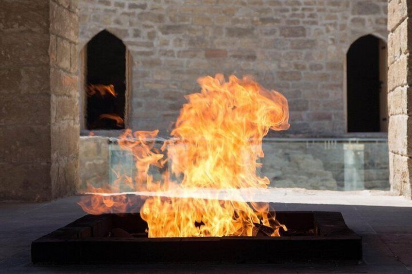 A fire burning in a metal container with stone walls and arched openings in the background. 3
