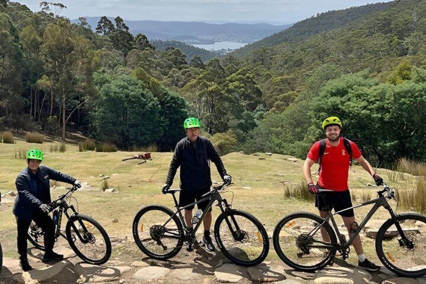 Three cyclists on a dirt path with a scenic view of a valley and hills in the background. 1