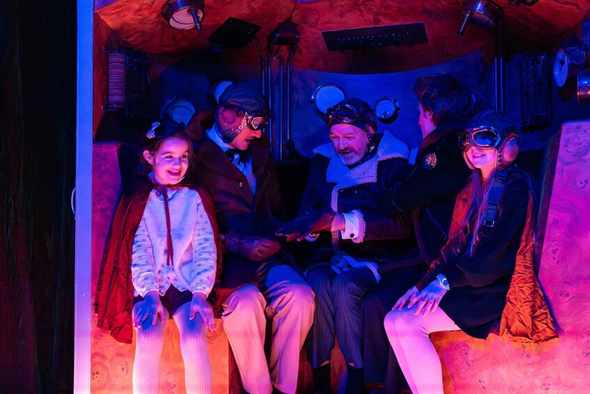 A group of people in vintage aviator attire seated in a room with wooden walls and vintage equipment. 3
