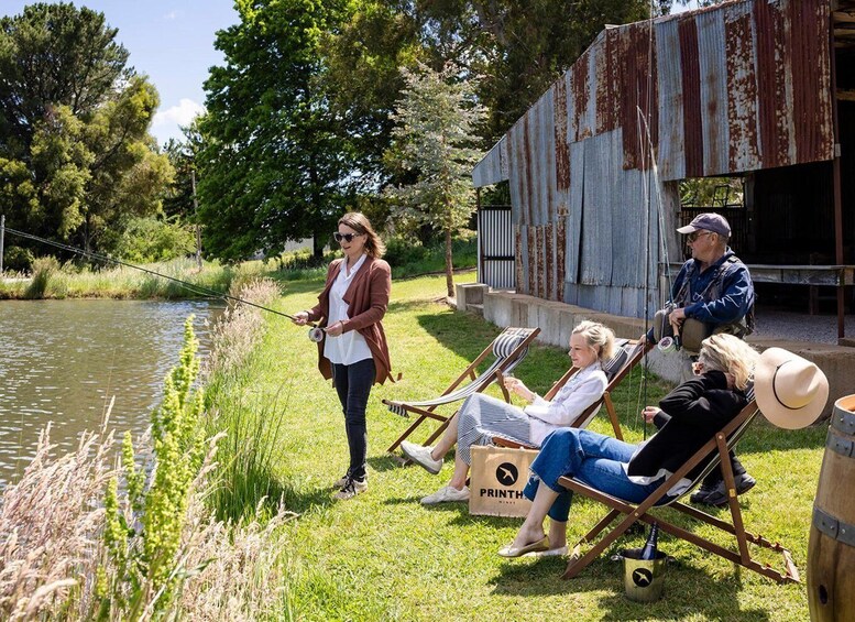 A group of people fishing by a river, with a rusted building in the background. 2