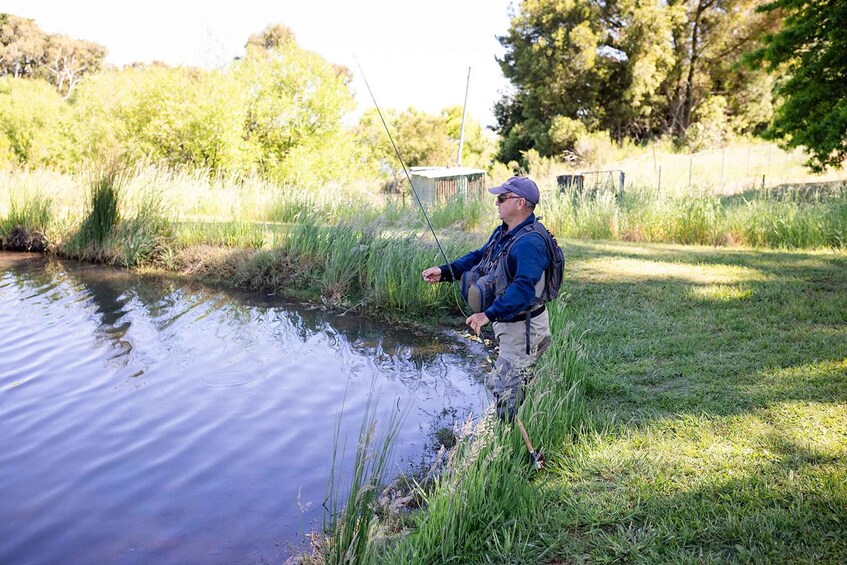A person fishing by a calm river with grass and trees in the background. 4