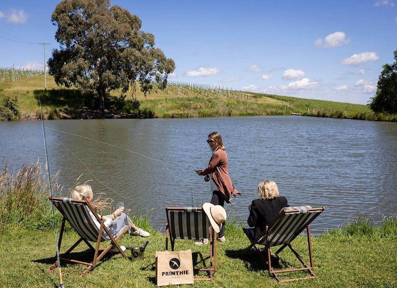 A lake with people fishing, chairs, and a sign for 'PRINTHIE WINES'. 3