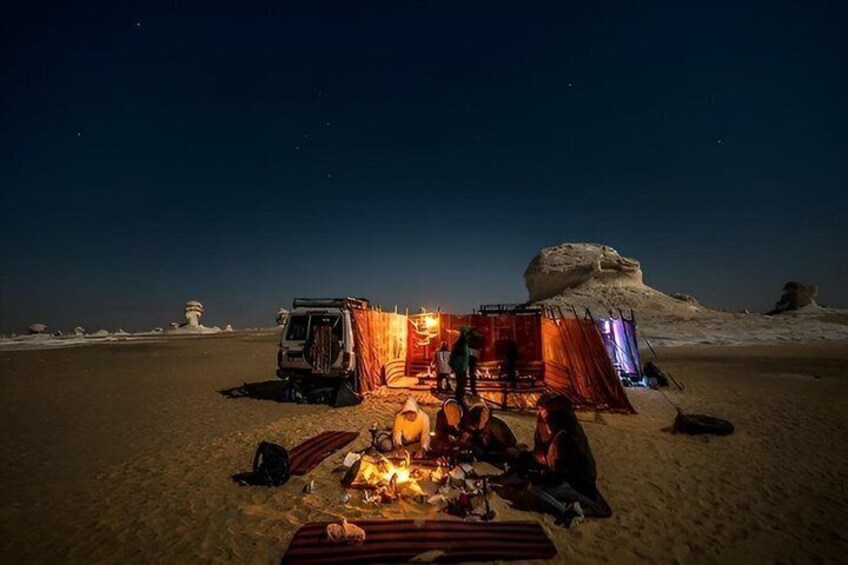 A desert campsite at night with tents, a vehicle, and a fire. 1