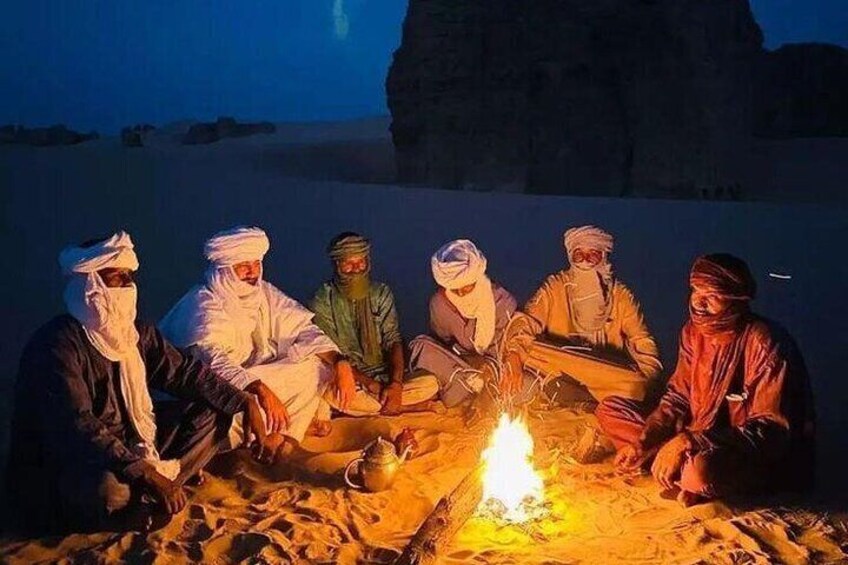 A group of people sitting around a campfire in a desert setting. 2