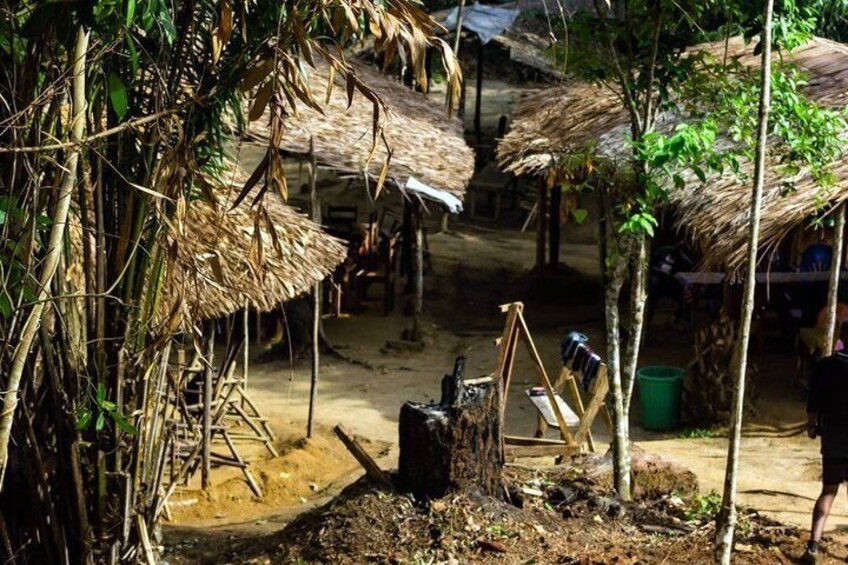 A rural village with thatched-roof huts, wooden structures, and a dirt path. 2