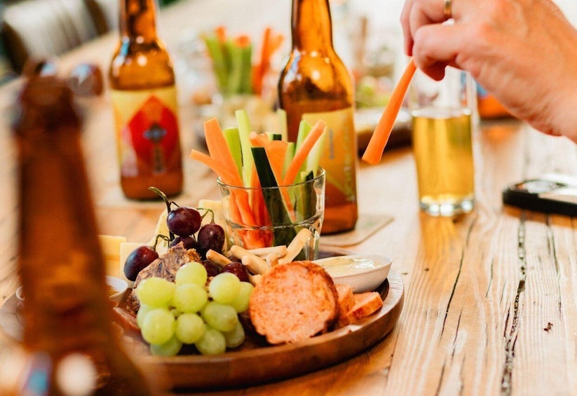 A wooden table with a charcuterie board, including grapes, cheese, and sliced meats, and a glass of beer. 1