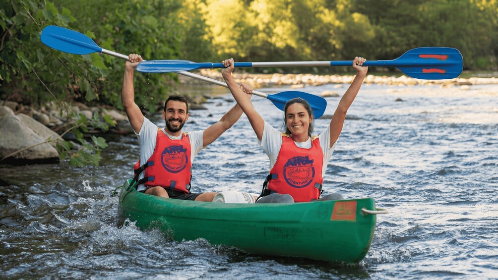 Two people kayaking on a river, wearing life jackets and paddling a green canoe. 3