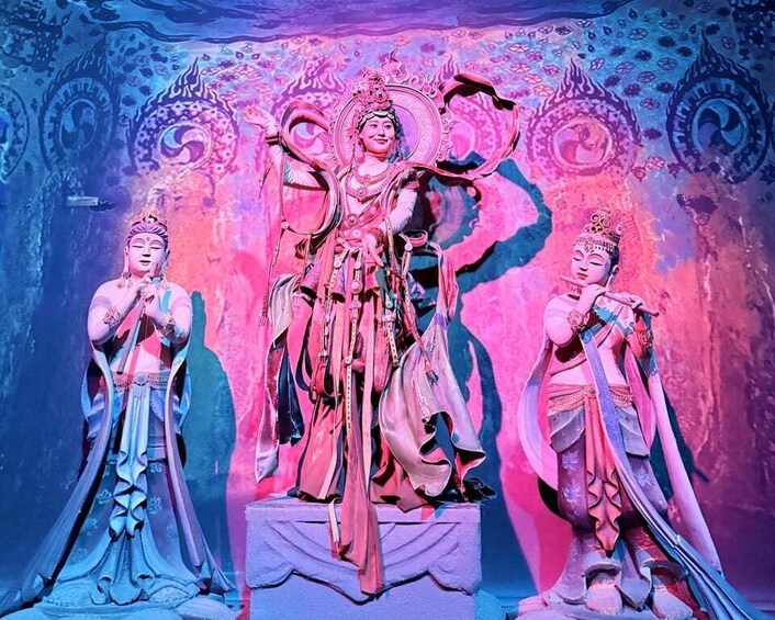 A statue of a deity with multiple arms, surrounded by smaller statues, set against a colorful, patterned backdrop. 3