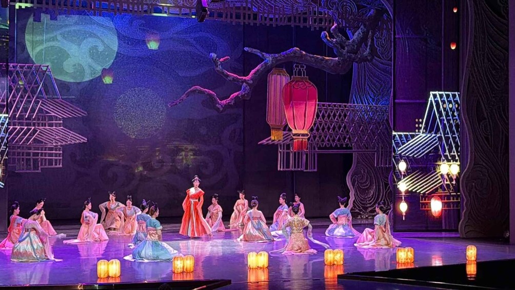 A stage with performers in traditional costumes, a large tree, and hanging lanterns. 5