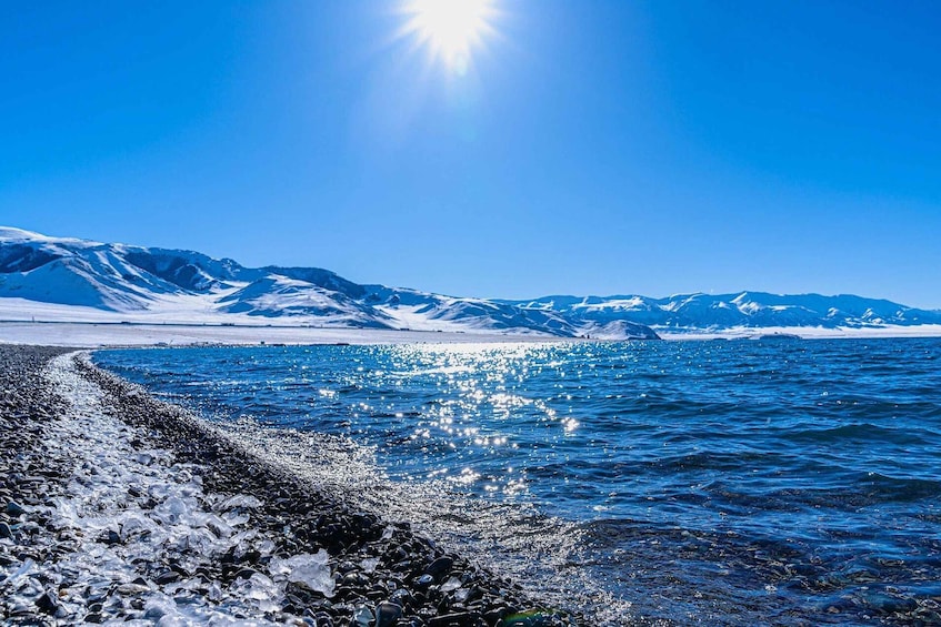 A glacier-topped mountain range, a rocky shoreline, and a calm sea under a clear sky. 2