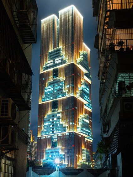 A modern skyscraper with illuminated windows and vertical wooden slats, surrounded by older buildings. 4