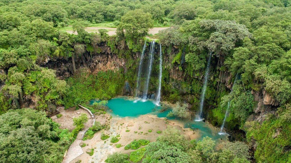 A waterfall cascading into a turquoise pool surrounded by dense forest. 2