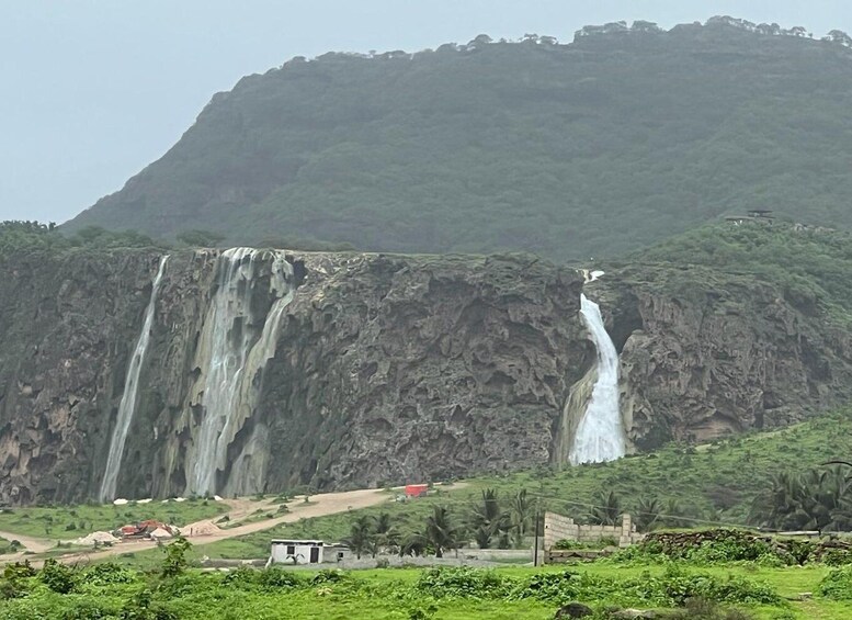 A waterfall cascading down a steep cliff, surrounded by lush greenery and a few scattered buildings. 3