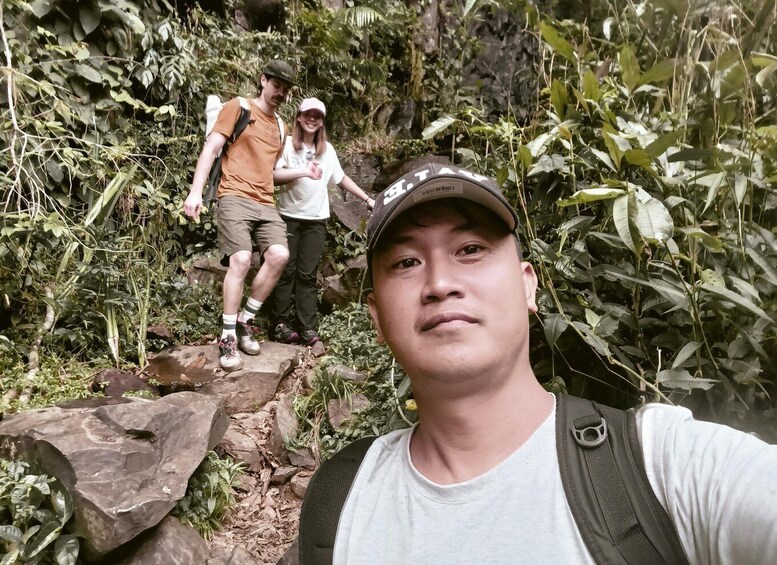A person taking a selfie with two hikers on a rocky trail surrounded by dense vegetation. 4