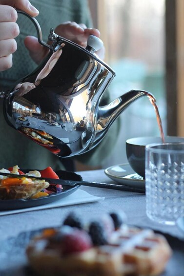 A person pouring tea from a shiny metal teapot into a cup. 3