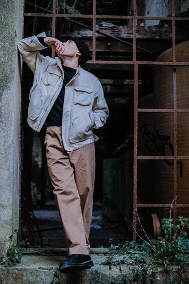 A person leaning against a metal gate, wearing a jacket and pants. 5
