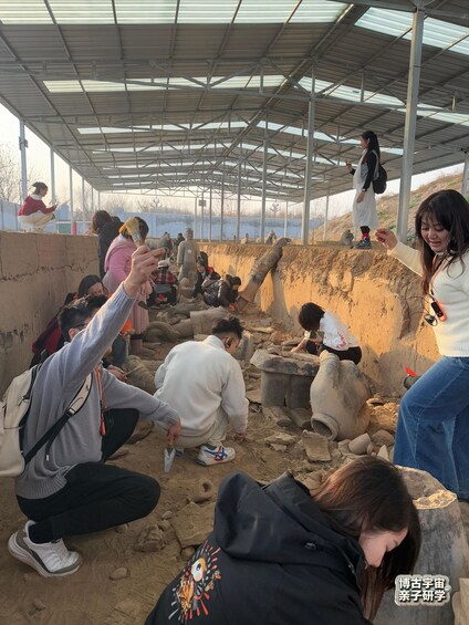 People examining ancient artifacts in an outdoor archaeological site with a metal roof structure. 2