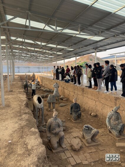 A group of people observing ancient terracotta figures in an outdoor museum setting. 3
