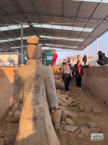An archaeological site with a large ancient statue, people walking around, and a covered shelter. 4