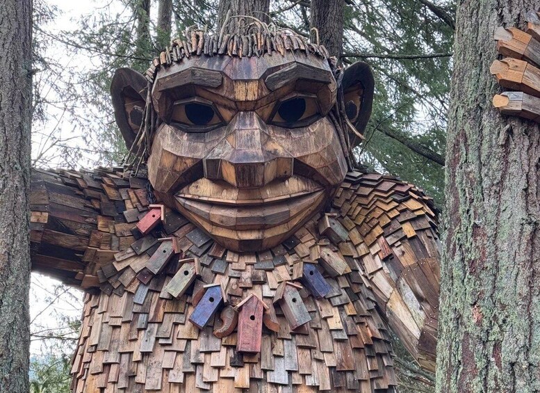 A large wooden sculpture resembling a face with outstretched arms, surrounded by trees. 4