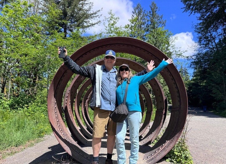Two people standing in front of a large circular metal sculpture. 3