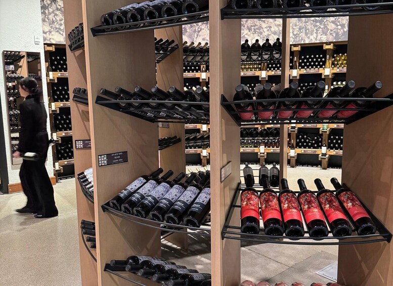 A wine store with shelves of wine bottles, a person browsing, and a sign indicating a 2019 artist series. 1