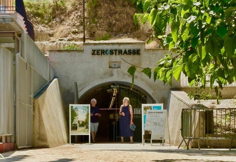 A tunnel entrance labeled 'ZERO STRASSE' with informational signs and a metal gate. 4