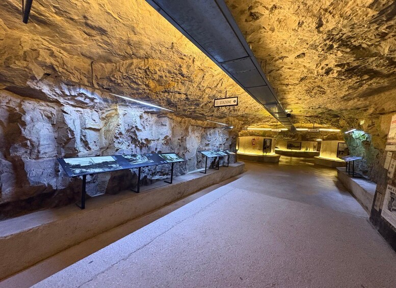 An underground museum with stone walls, exhibits, and a central walkway. 3