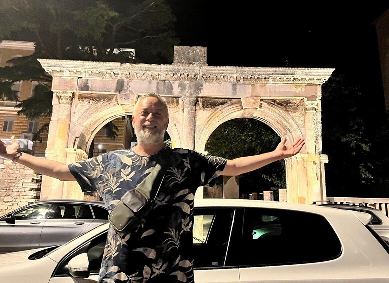 A person standing in front of an ancient stone archway with arms outstretched. 1