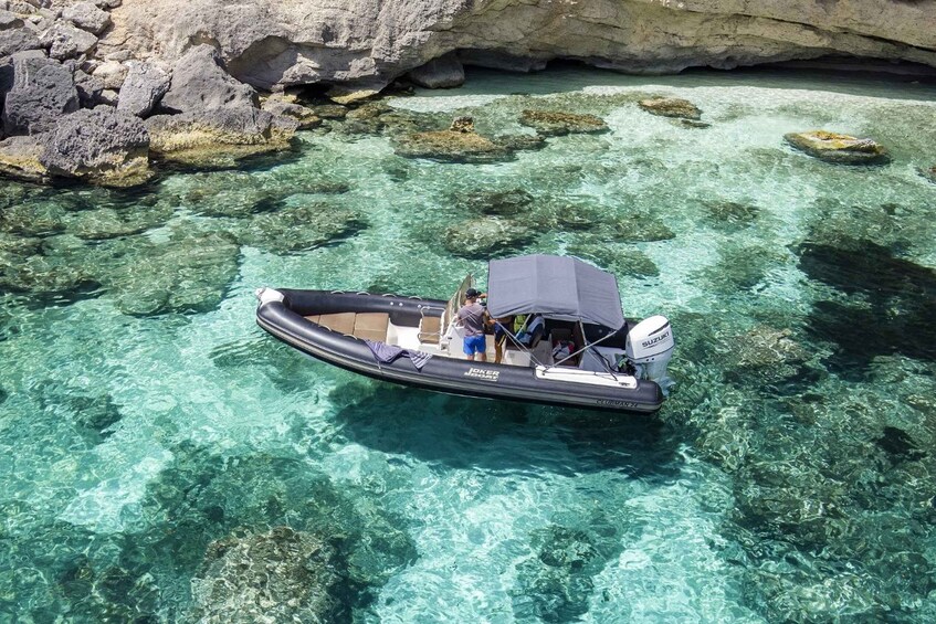 A boat with a canopy and a Suzuki outboard motor on clear turquoise water near rocky formations. 1